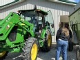 2 young women looking at a John Deere tractor with another young woman in the driver's seat